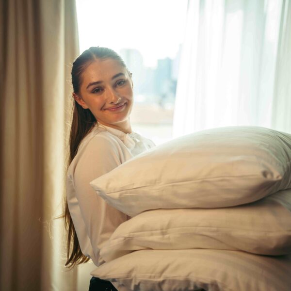 A smiling roommaid holding pillows infront of a window